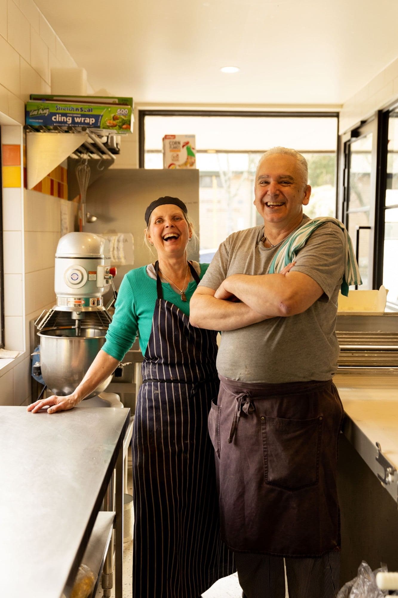 Two bakers laughing in the bakery kitchen beside the mixer